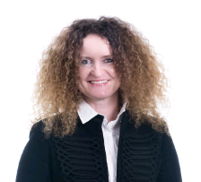 Legal professional with curly hair wearing a black jacket, smiling, in a neutral setting.