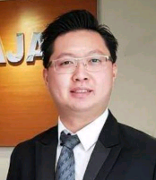 Lawyer standing in front of a law firm sign, wearing a suit and glasses.