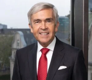 Senior attorney posing confidently in office setting with cityscape backdrop.