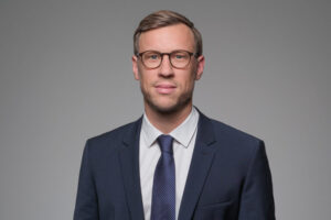Male lawyer wearing glasses in a suit with a neutral background.