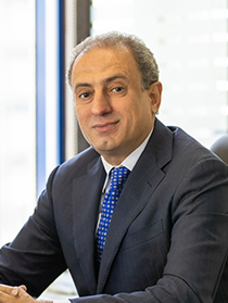 Lawyer seated at desk in office, wearing a suit with a confident expression. Natural light from window.