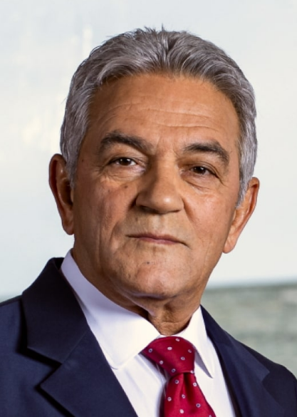Senior attorney in a suit, positioned against a blurred coastal background.