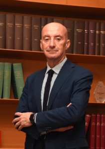 Lawyer posing confidently with arms crossed in front of legal books, showcasing a professional library setting.