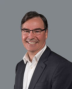 Business professional smiling in a suit against a neutral background.