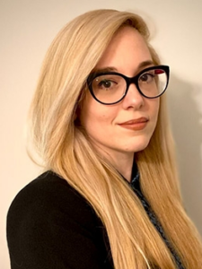 Legal professional with long blonde hair and glasses, looking directly at the camera in a neutral setting.