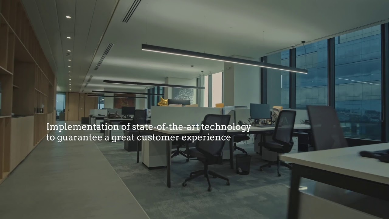 Modern office workspace featuring desks, computers, and large windows with a city view.
