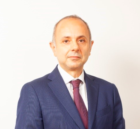 Attorney in professional attire, standing against a plain background, conveying a formal and approachable demeanor.
