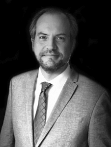 Lawyer in a suit, standing confidently with a neutral background, presenting a professional image.