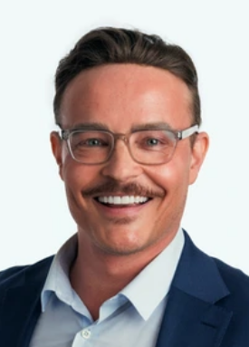 Smiling man in a suit and glasses, posing against a plain background.