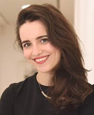 Smiling woman with long dark hair wearing a black top, positioned in a professional environment.