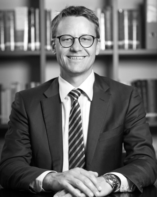 Lawyer smiling confidently at desk with legal books in background, suggesting a professional legal environment.