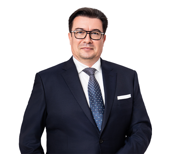 Lawyer in a suit with glasses, standing confidently against a neutral background.