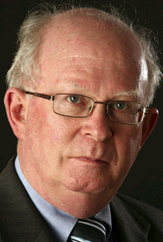 Lawyer with gray hair and glasses, looking directly at the camera against a dark background.