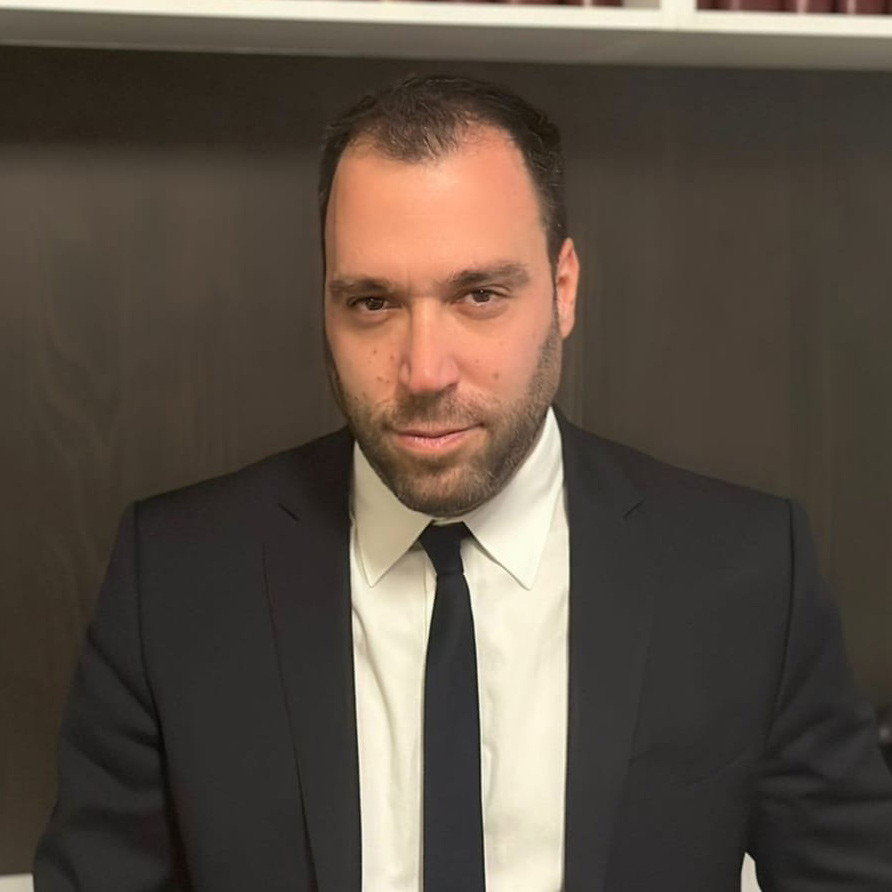 Lawyer in a suit posing confidently in an office setting with legal books in the background.