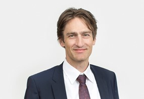 Lawyer in a suit with a confident expression, posing for a professional portrait against a neutral background.