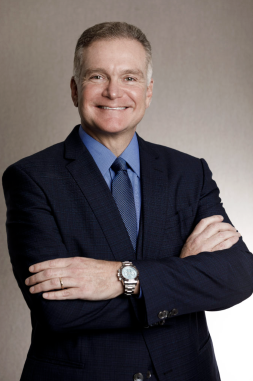 Attorney smiling with arms crossed, wearing a suit, against a neutral background.