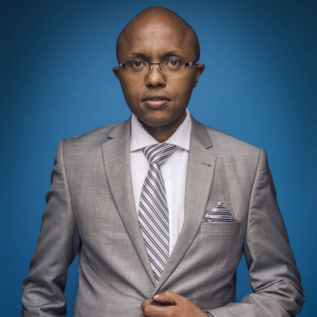 Lawyer in gray suit with striped tie, standing confidently against a blue background.