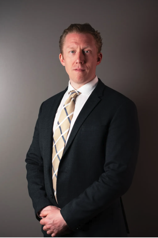 Attorney in formal attire standing confidently against a neutral background.