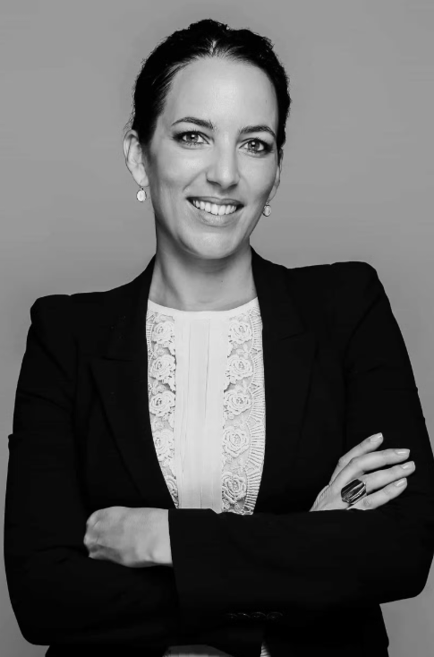 Professional woman in business attire smiling with arms crossed, against a neutral background.