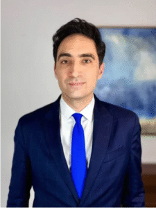 Legal professional in a blue tie and dark suit, standing in an office setting with a neutral background.