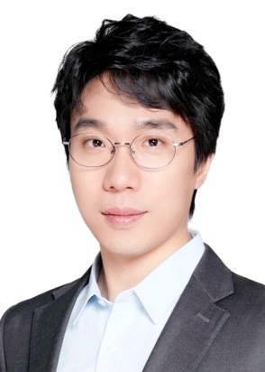 Professional individual with glasses in a suit, posing for a portrait against a plain background.