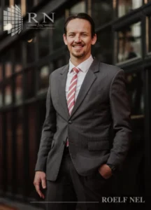 Professional in a suit standing confidently against a modern glass backdrop.