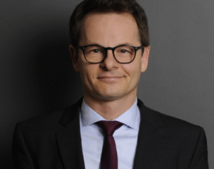 Lawyer in a suit with glasses, smiling in a professional studio setting.