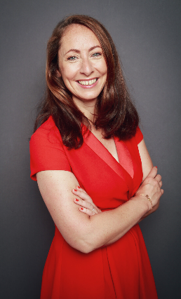 Smiling professional in a red dress with arms crossed, posing against a neutral background.
