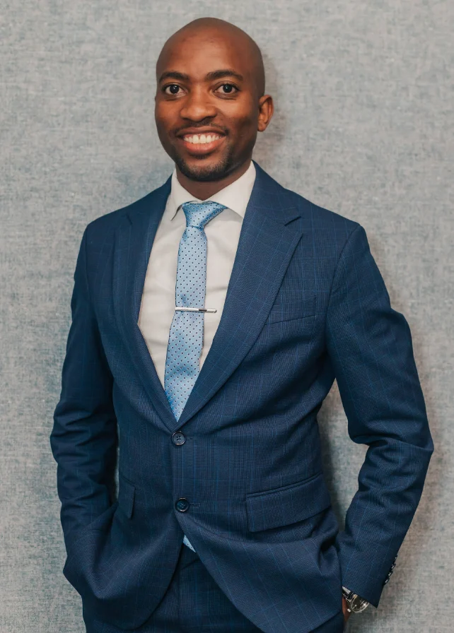 Attorney in a blue suit with a light tie, smiling against a textured gray background.