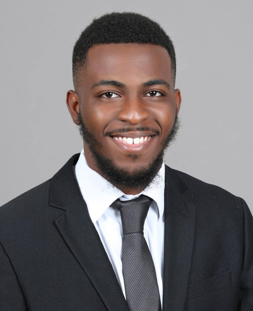 Professional man in a suit with tie smiling against a plain background.