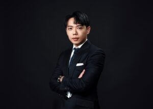 Attorney in formal suit standing confidently with arms crossed against a dark backdrop.