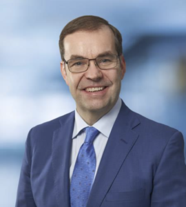 Smiling attorney in a blue suit, standing against a soft-focus background.