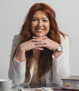 Lawyer smiling and resting hands on a desk, with legal books and a pen visible in a professional setting.