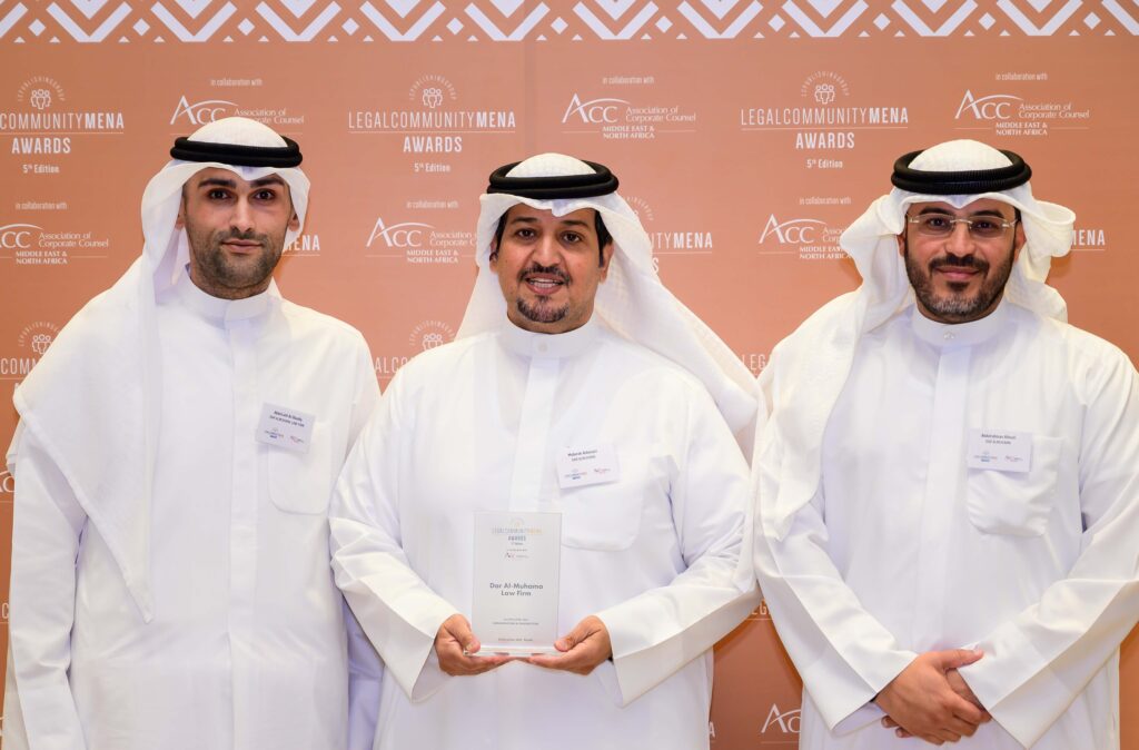 Legal professionals holding an award plaque at the Legal Community MENA Awards event backdrop.