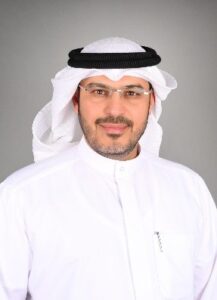 Male attorney in traditional attire, smiling against a neutral gray background.