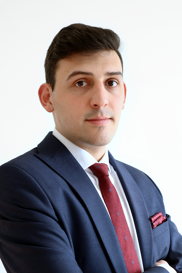 Lawyer in a business suit, standing with arms crossed, against a plain background.
