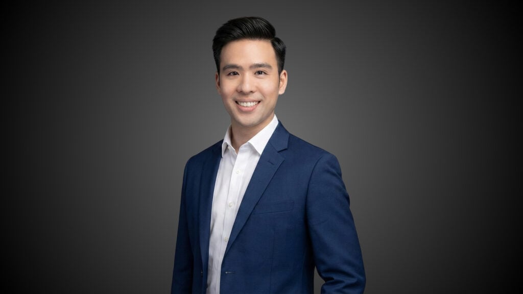 Professional man in a suit smiling against a dark background.