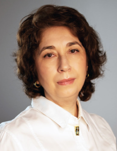 Legal professional with shoulder-length hair, wearing a white blouse, posed against a neutral background.