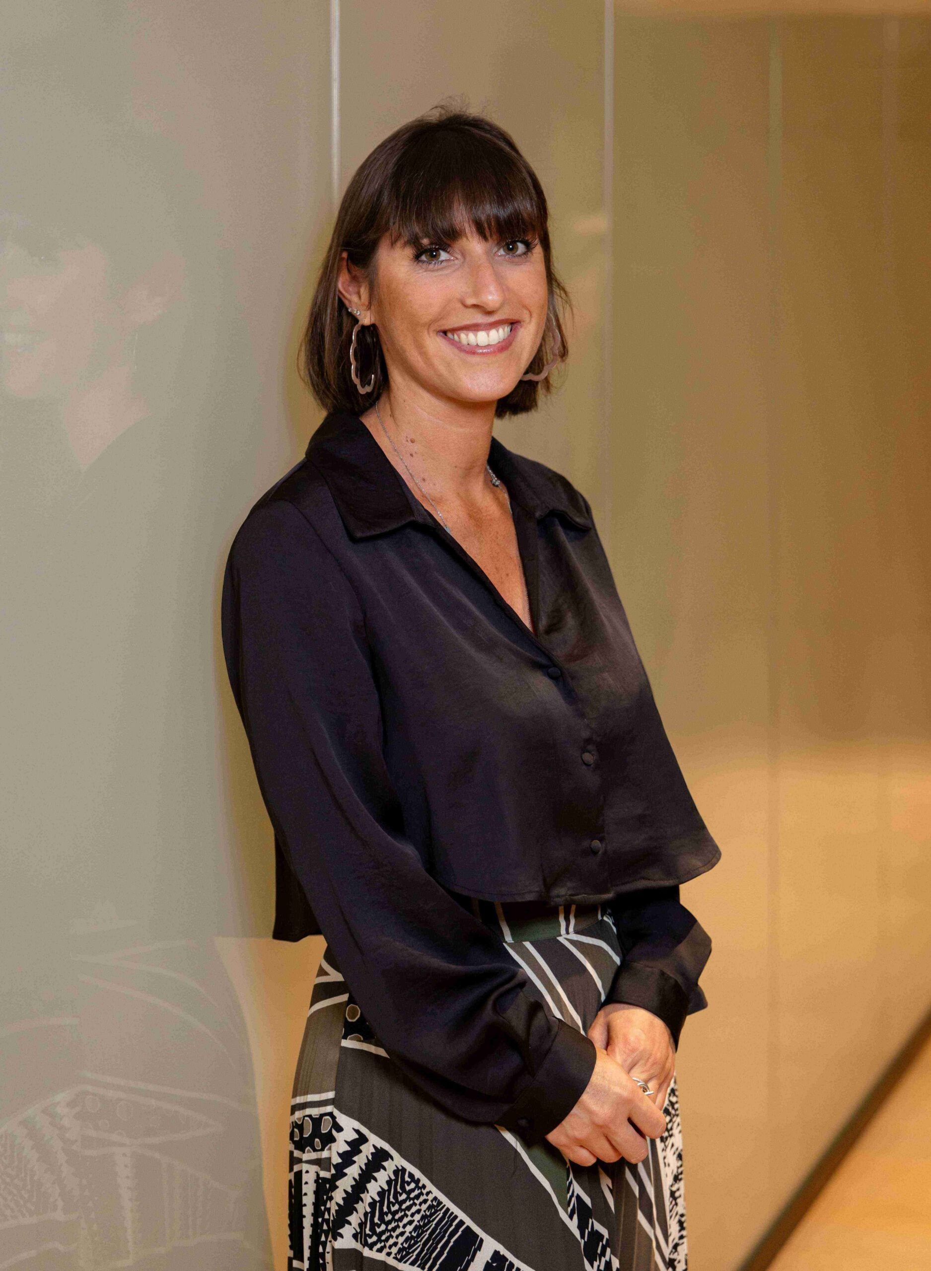Legal professional smiling while standing against a modern office wall in a business attire.