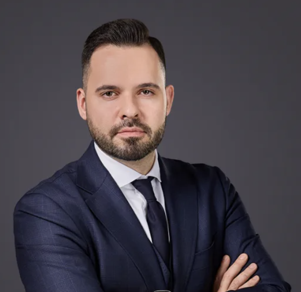 Attorney posing confidently with arms crossed, dressed in a formal suit against a neutral backdrop.