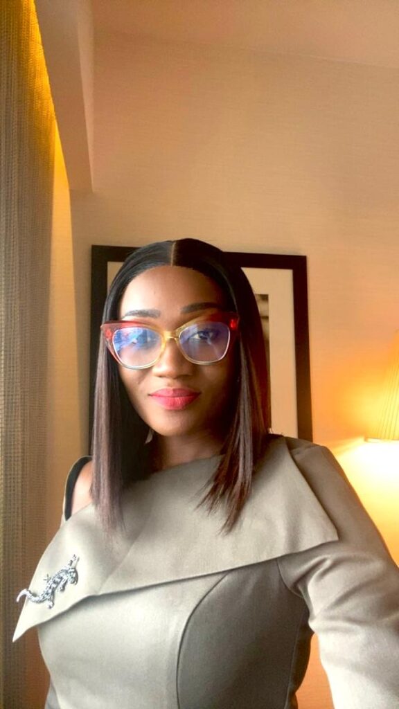 Business professional posing for a selfie in a well-lit indoor setting, wearing stylish glasses and a modern outfit.