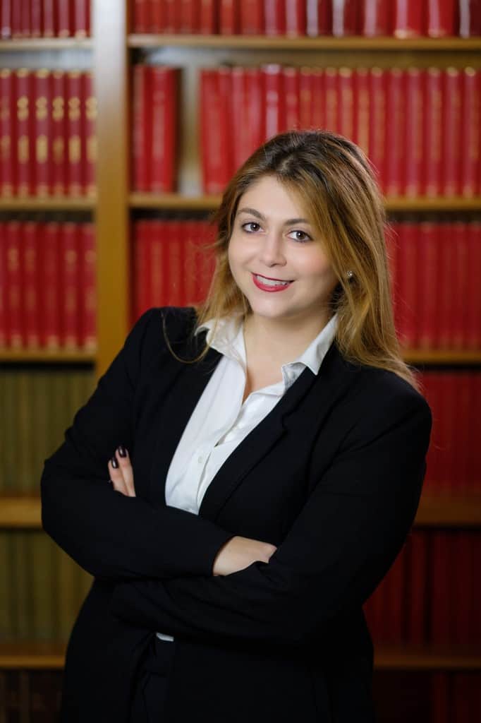 Lawyer standing confidently with arms crossed in front of a bookshelf filled with legal texts.