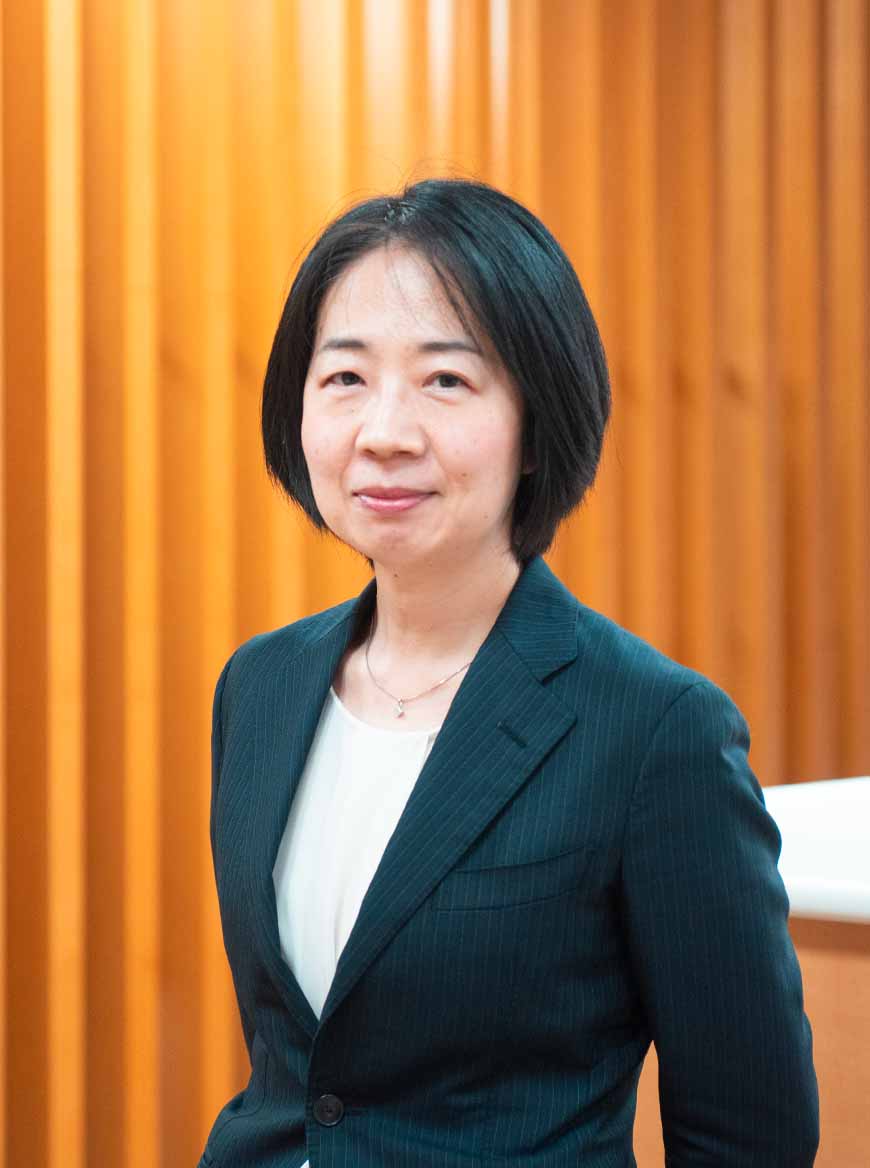Lawyer in a professional suit standing in a modern office setting with wooden paneling in the background.