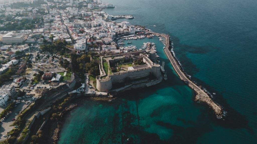 Aerial view of coastal town featuring a historic fortress, marina, and vibrant waterfront with clear blue water.