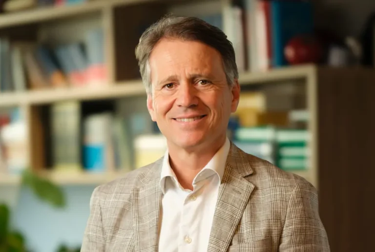 Legal professional smiling at the camera in a law office with bookshelves and legal materials in the background.