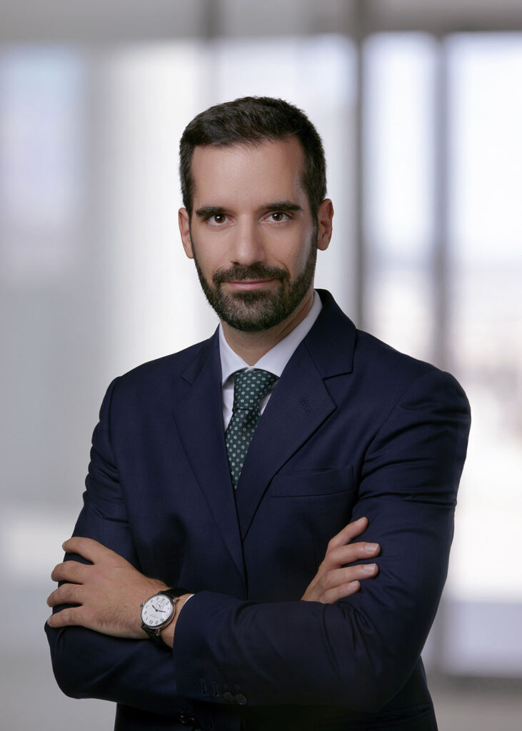 Professional man in a suit with crossed arms, standing in a modern office setting.