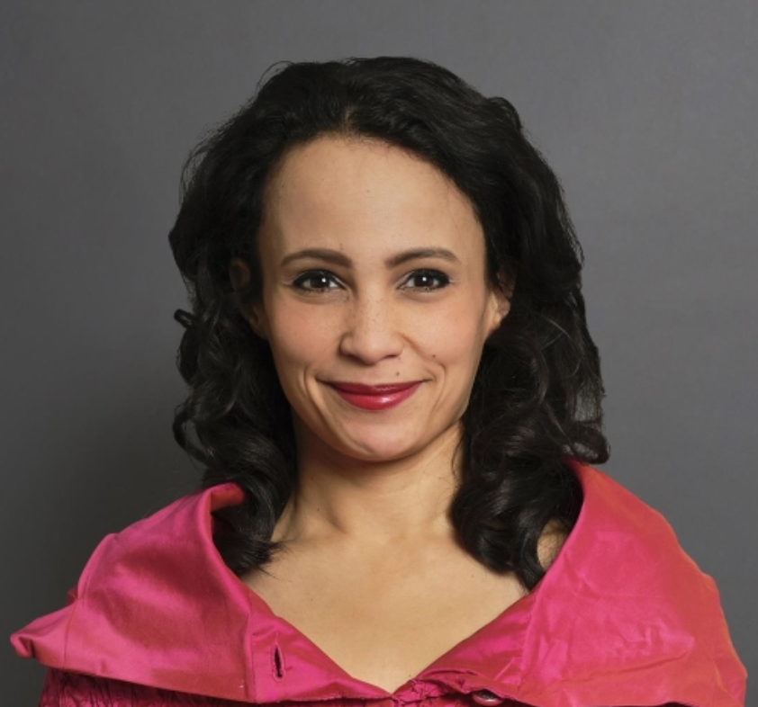 Legal professional with dark, curly hair, wearing a pink shawl, posing for a portrait against a neutral background.