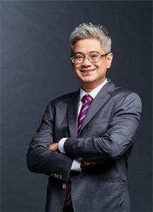 Legal professional standing confidently, arms crossed, wearing a suit and tie against a neutral background.