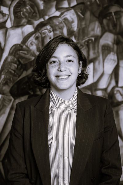 Legal professional smiling in front of an artistic backdrop, dressed in a suit, conveying a confident demeanor.