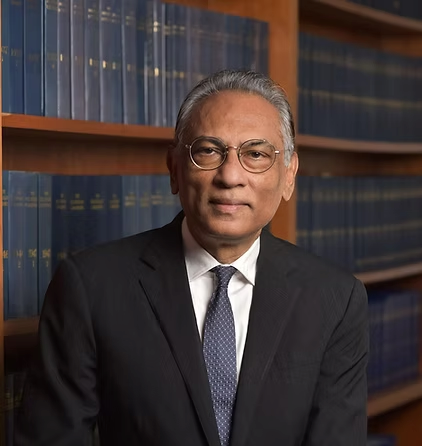 Lawyer posing confidently in a suit, with legal books visible on shelves in the background.
